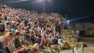 Large audience seated in outdoor stepped seating watching a night performance at the Getty Villa in Los Angeles