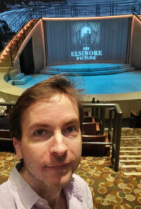 ethan hulbert sitting in the mark taper forum with hamlet stage behind him