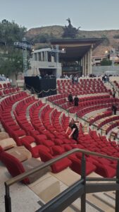 Red cushioned seats arranged in a semicircle inside Getty Villa amphitheater with staff preparing before an event, hills in background