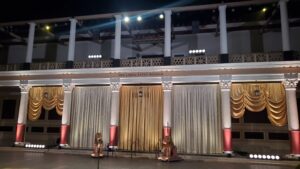 Classical stage at Getty Villa with tall white columns and gold and cream curtains lit by warm spotlights at night