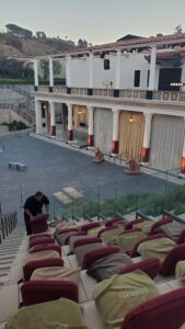 Theater seating at Getty Villa with red chairs covered by reserved cloths and a person arranging cushions before a performance