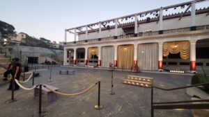 Outdoor theater stage at Getty Villa with columns, beige curtains, and scattered chairs and microphones under twilight sky