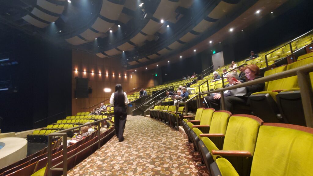 A right-looking view inside the Mark Taper Forum theater, showing the seats and stage and aisles and stairs and usher.