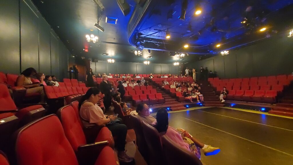 Interior of the Nocturne Theater showing seating and audience looking towards the front doors and front side.