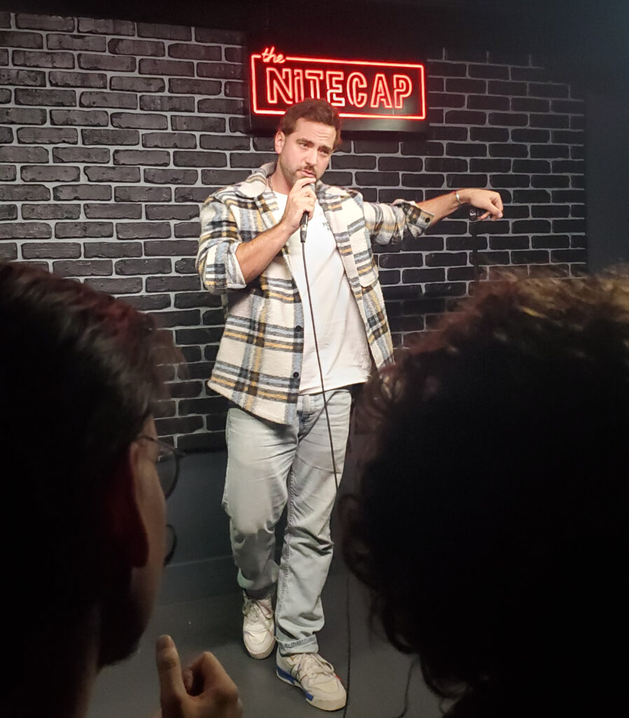 pat quinn comedian - a man doing stand up comedy in front of a black brick wall