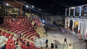 Theater venue with red seats and people preparing the stage and audience area at night under artificial lights