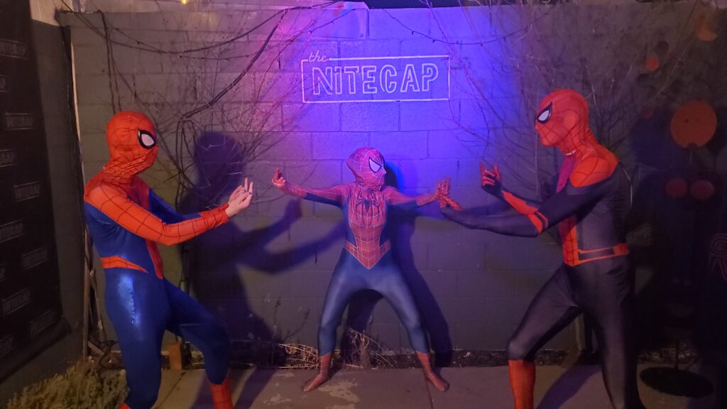 Three people in spider-man halloween costumes flipping each other off, all three giving the others middle fingers